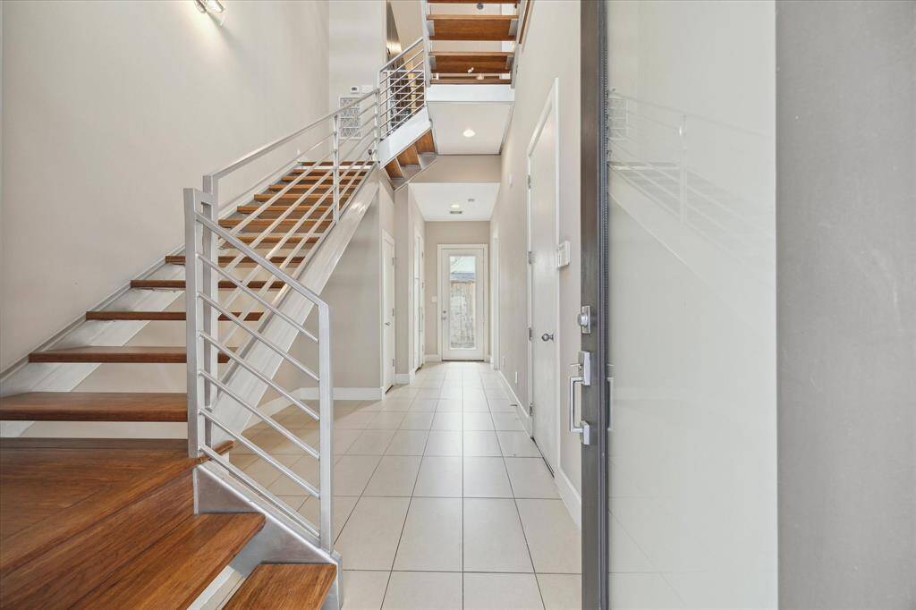 Bright, inviting entrance with a modern floating staircase leading to the family room and kitchen. A bedroom is tucked away to the right at the end of the entryway.