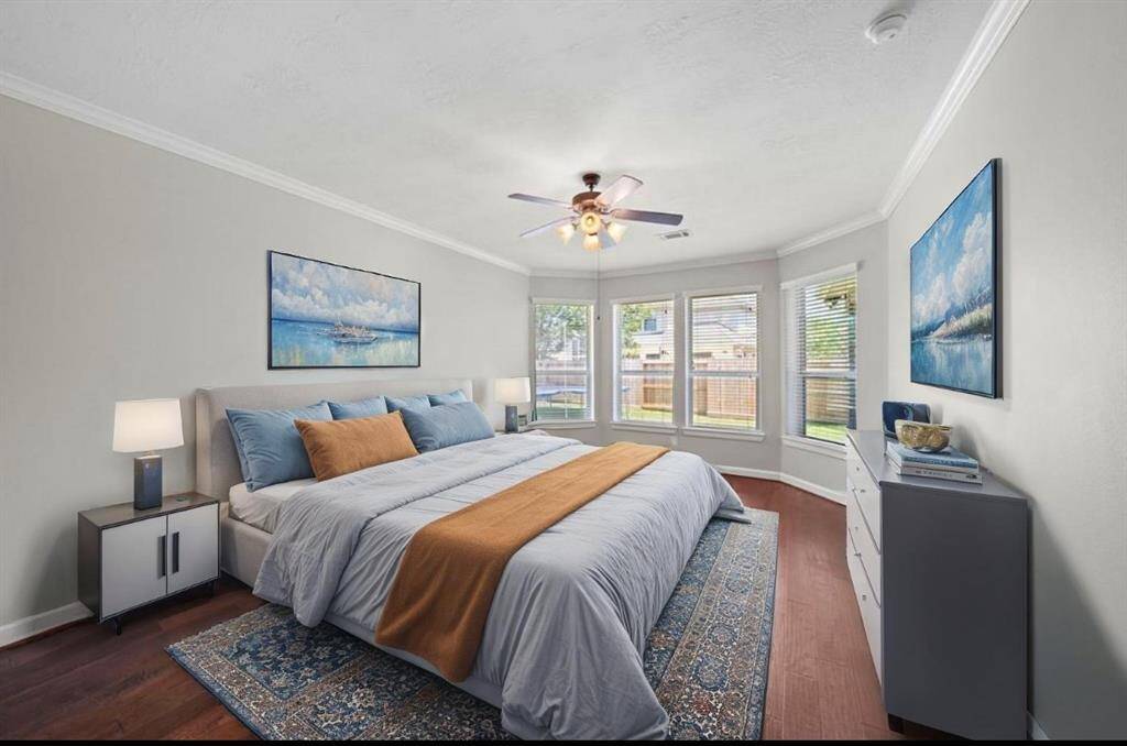 Large primary bedroom with warm hardwoods and natural light, virtually staged.