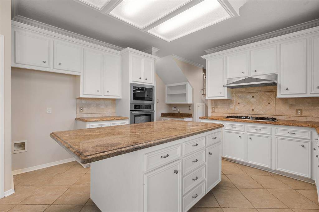 Updated kitchen features white cabinetry, a large granite island, and modern built-in appliances. It offers ample storage and counter space, perfect for cooking and entertaining. The light tile flooring and neutral tones is perfect for the chef!