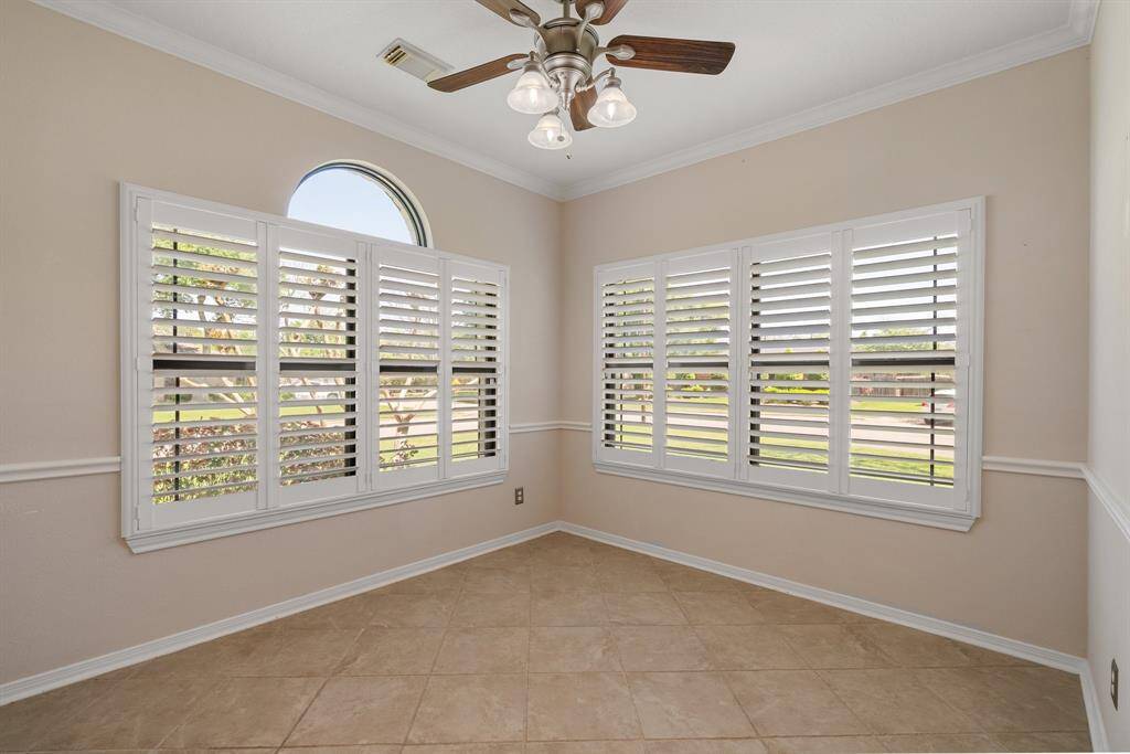Bright room with large windows featuring white shutters, neutral walls, and tiled flooring. Ceiling fan adds comfort and style. Ideal for dining or a sunroom.