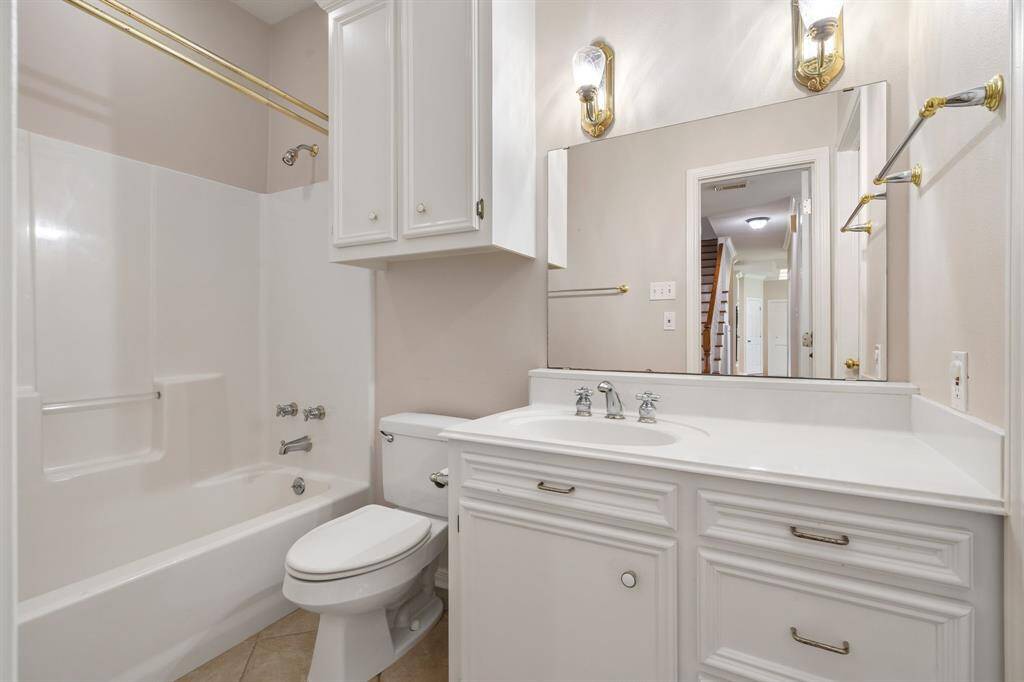 Downstairs bathroom features a clean, classic design with white cabinetry, a bathtub, and a large mirror. It has brass accents, overhead lighting, and ample storage space.