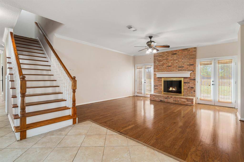 Living area features beautiful hardwood floors, a cozy brick fireplace, and abundant natural light from large windows and French doors. The open stairway adds elegance and leads to the upper level, enhancing the room's inviting atmosphere.