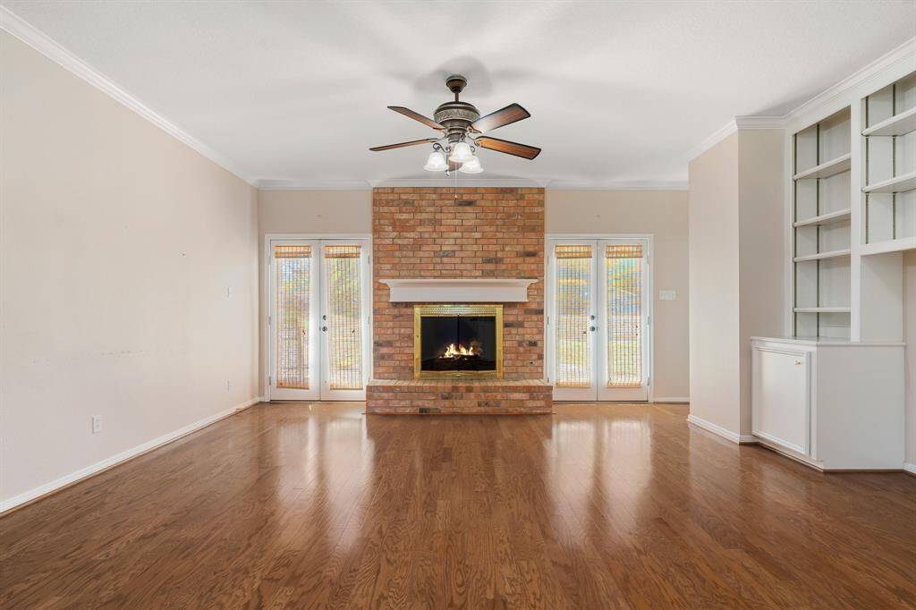 Living area with a cozy brick fireplace, hardwood floors, and built-in shelving. French doors on either side of the fireplace bring in natural light, while a ceiling fan adds comfort.
