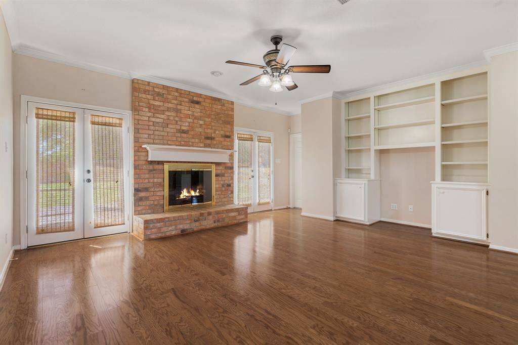 Living room features hardwood floors, a central brick fireplace, built-in shelving, and large windows with door access to the outside, allowing natural light to fill the space.