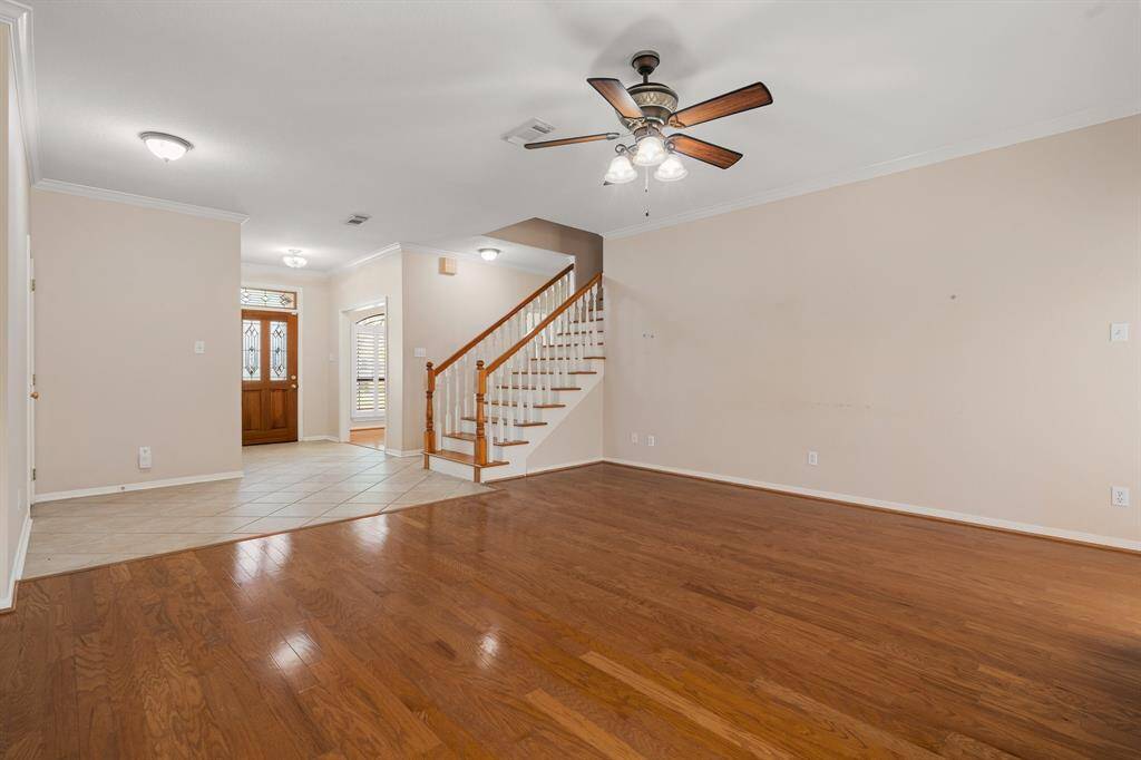 Living area features warm hardwood floors, a ceiling fan, and neutral walls. It opens to an entryway with tile flooring and a wooden staircase, creating a welcoming and versatile space perfect for personal touches.
