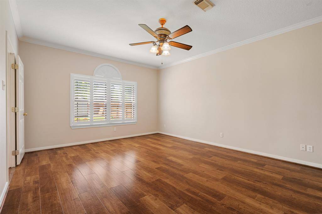 Neutral primary bedroom features warm wood flooring, a ceiling fan, and a large window with shutters that provide plenty of natural light. The neutral walls offer a versatile backdrop for any decor style.