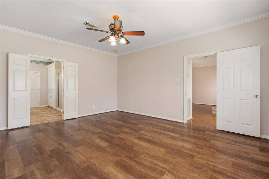 Primary bedroom has ample natural light and offers access through double doors to an adjacent room with tile flooring, as well as another doorway leading to a room with hardwood flooring.