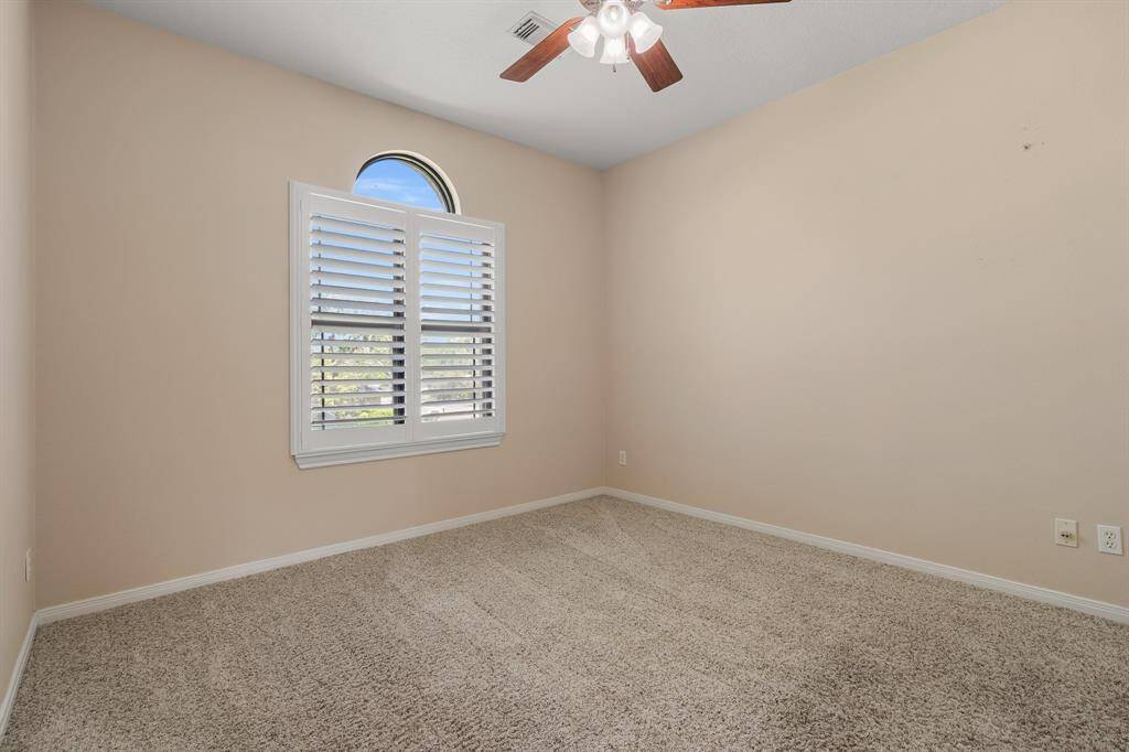 Second bedroom features soft beige walls, carpeted flooring, a ceiling fan with lights, and a window with plantation shutters that allow natural light!