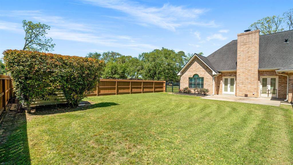 A spacious backyard with a well-maintained lawn, privacy fence, and a brick exterior home featuring a cozy patio area. Perfect for outdoor activities and relaxation.