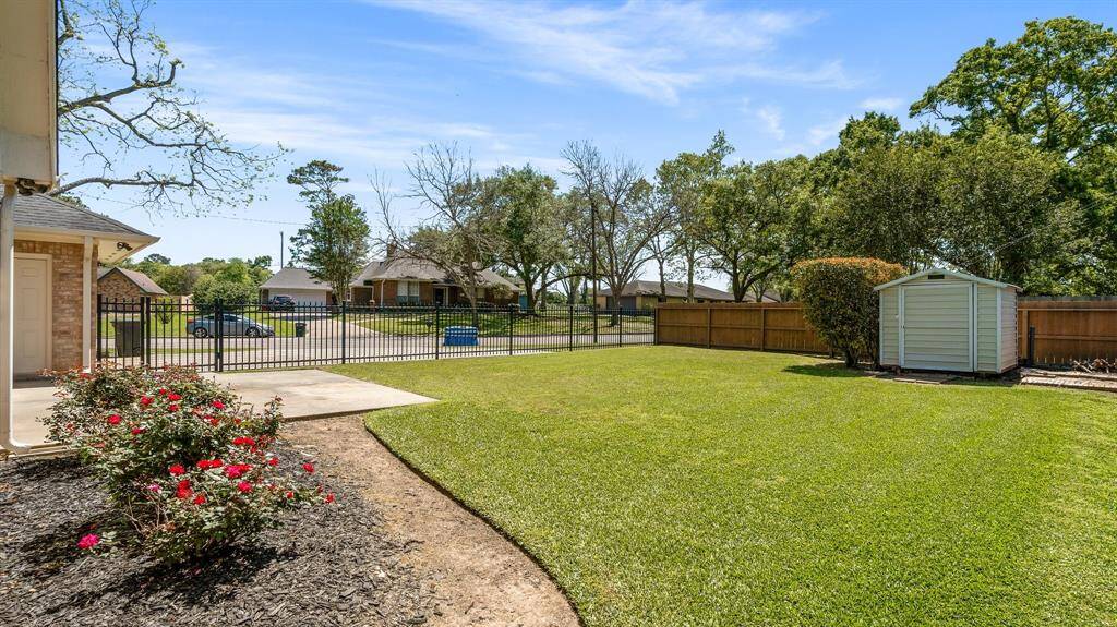 Stop and smell the roses!  A flower bed with vibrant red roses is enclosed by a fence, offering privacy and security, with a view of a quiet neighborhood street.