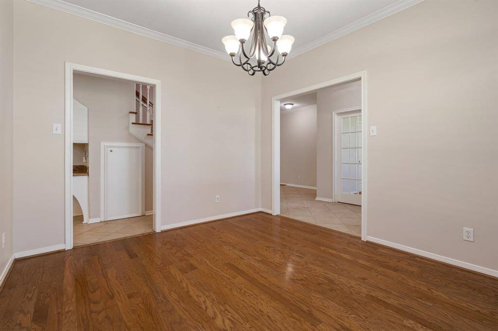 Bright formal dining room with hardwood floors, neutral walls, and a stylish chandelier. It features two doorways, one leading to the kitchen and the other to an office with glass-paned doors.