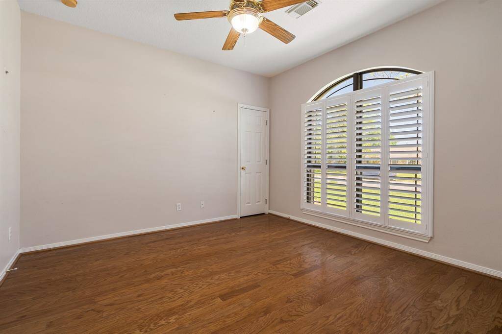 Office or study features hardwood flooring and a large arched window with plantation shutters, providing plenty of natural light. It also includes a ceiling fan and a neutral color scheme, creating a bright and airy space.