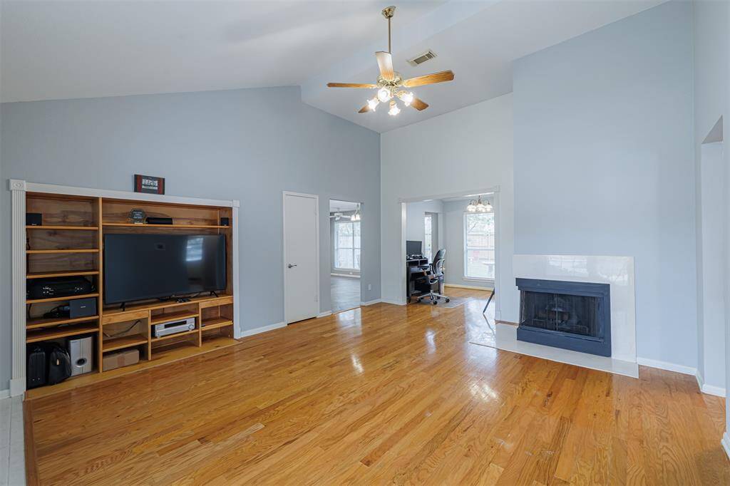 A generous family room featuring soaring ceilings, wood flooring, a cozy fireplace, and a custom built-in entertainment center.
