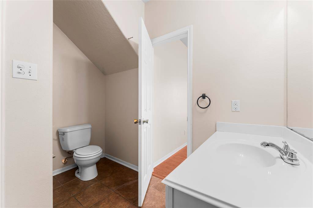 This photo shows a small, clean bathroom with a white vanity, under-the-stairs toilet area, and tile flooring. Neutral walls and simple fixtures create a functional space.