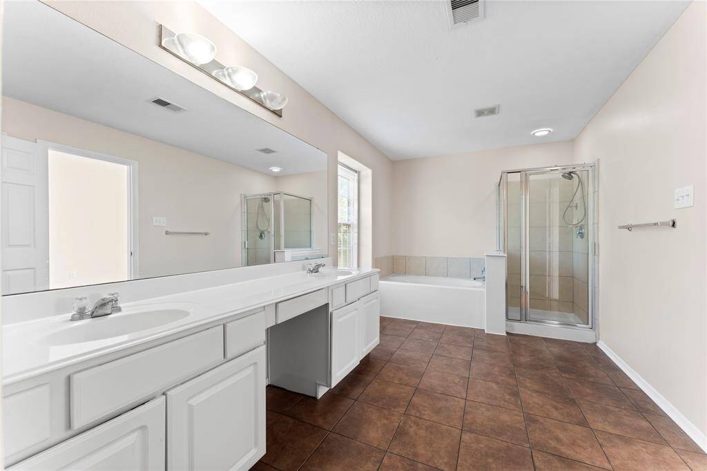 This spacious bathroom features a large double vanity with ample storage, a soaking tub, a glass-enclosed shower, and natural light from a window, all set against neutral tones for a modern feel.