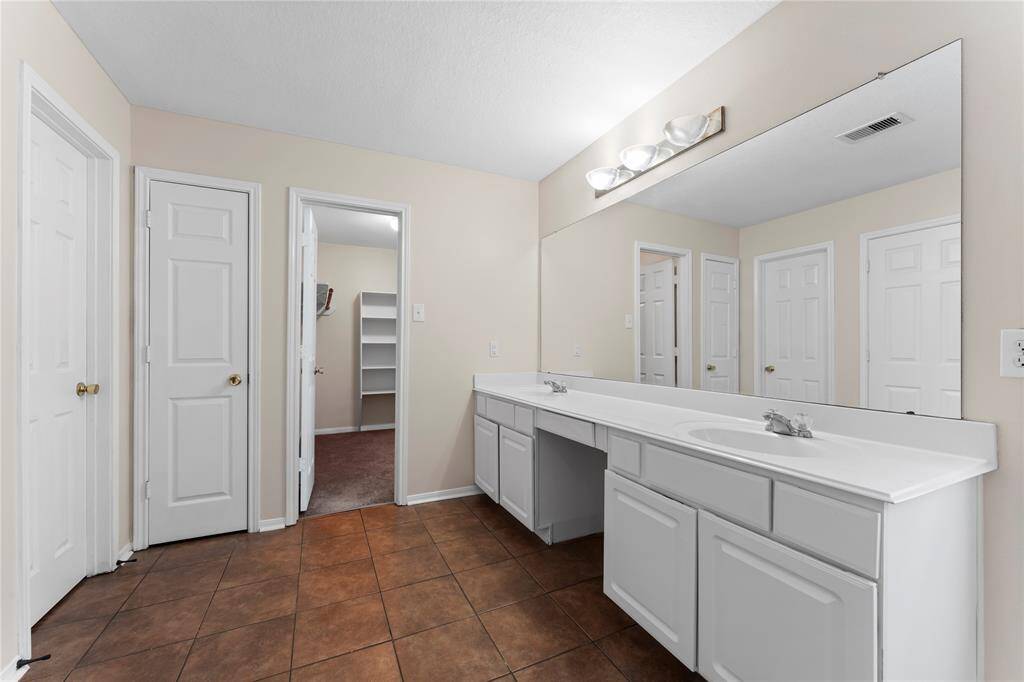 Spacious bathroom with dual sinks, large mirror, and neutral tile flooring.