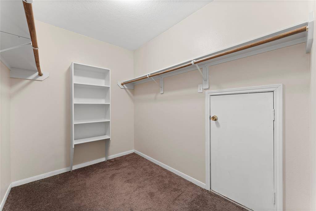 This is a spacious walk-in closet featuring carpeted flooring, built-in shelving, and ample hanging space.