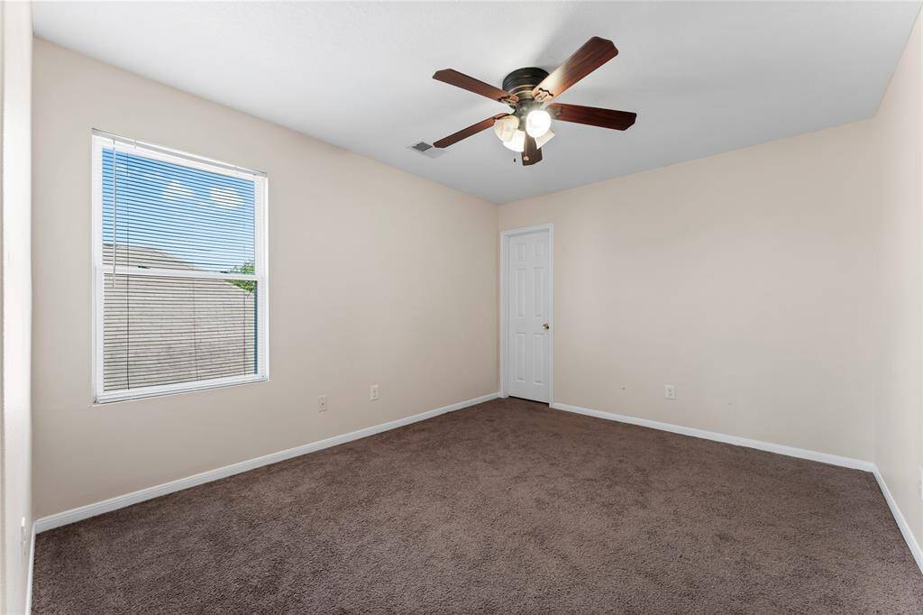 This room features neutral walls, a ceiling fan with lights, brown carpet, and a window providing natural light.