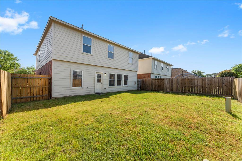 This photo shows the backyard of a two-story house with a well-maintained lawn, surrounded by a wooden fence, providing privacy and outdoor space.