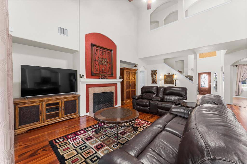 The living room features a stunning central fireplace, soaring ceilings open to the upstairs catwalk, and warm wood laminate flooring that adds charm and character.