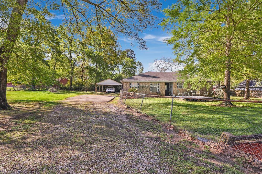 This charming brick home features a spacious front yard with a large tree providing shade, a wooden deck for outdoor seating, and is completely fenced, offering a great outdoor space for relaxation.