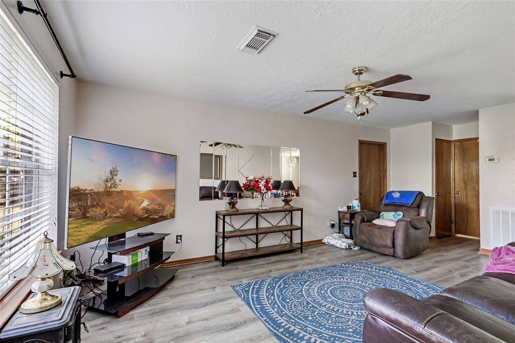 This living room features woodgrain flooring, a ceiling fan, and ample natural light from large windows.