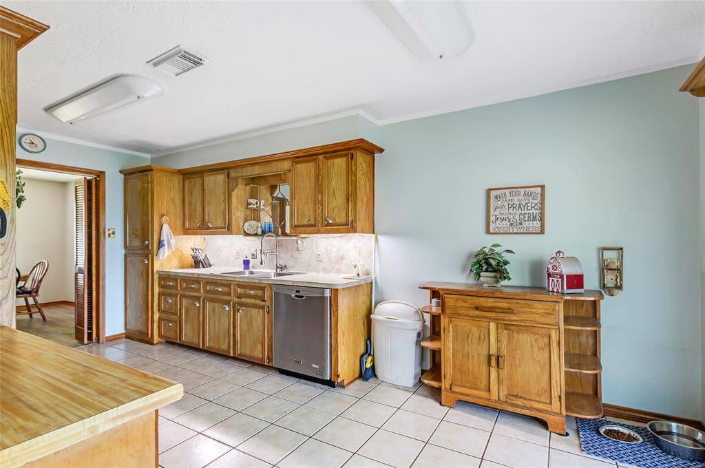 This kitchen features classic wooden cabinetry, ample counter space, and a double sink. It has tile flooring and a large sliding glass door that offers plenty of natural light. The area includes modern appliances, making it functional and inviting.