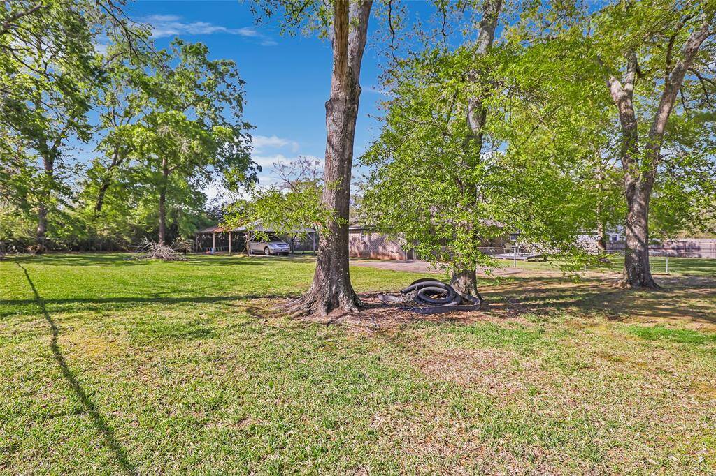 Charming single-story home with a brick exterior, nestled among mature trees. It features a spacious yard, driveway, and a large carport. Perfect for those seeking a serene, natural setting.