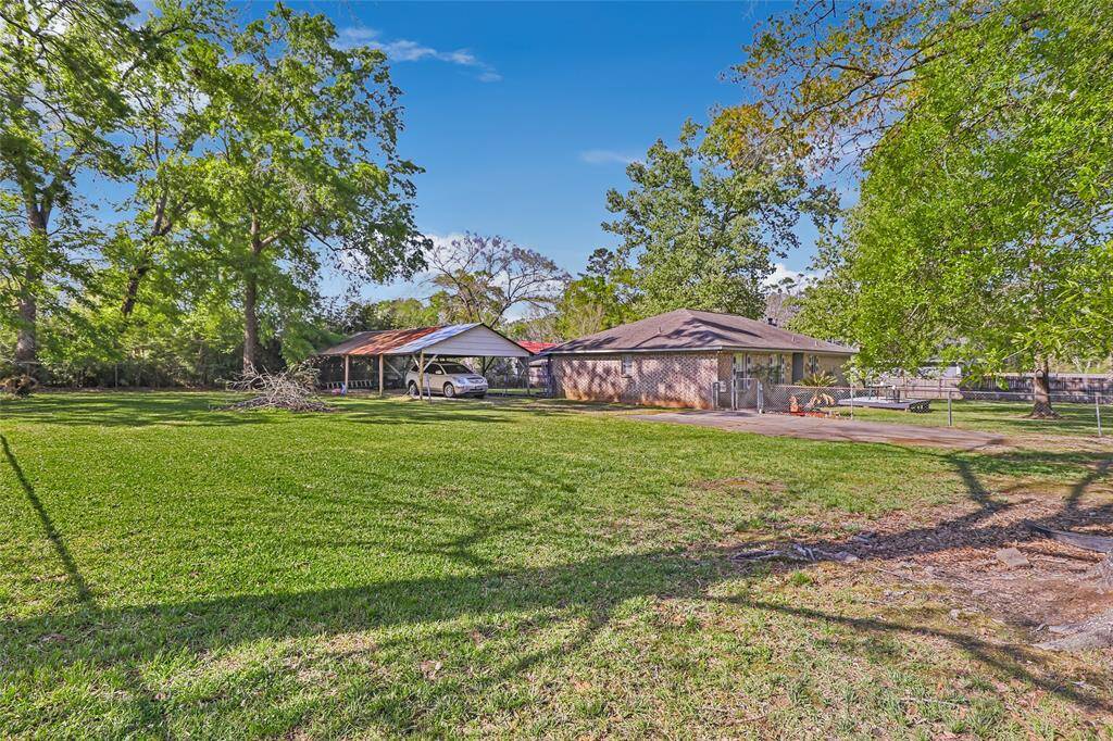 Spacious yard with 3 lots and lush green grass and mature trees, providing shade and a tranquil setting. A house and a carport are visible in the background, suggesting ample outdoor space for activities and parking. Ideal for those seeking a serene, natural environment.