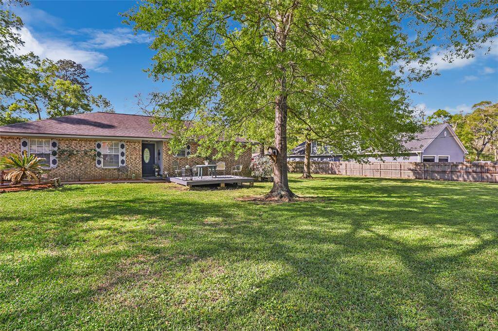 This photo shows a single-story brick house with a spacious yard, surrounded by mature trees. There's a large covered carport, and the property is bordered by a fence, offering a serene and private outdoor space.