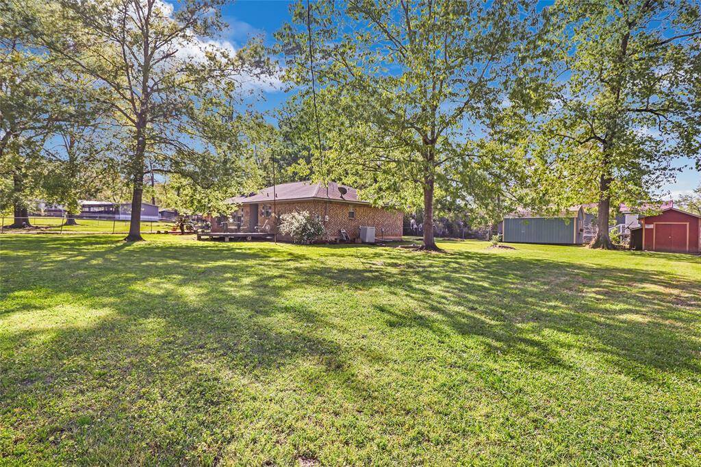 Another view of front yard with lush green lawn, mature trees providing shade, and a brick house featuring a patio area. Ideal for outdoor activities and relaxation.