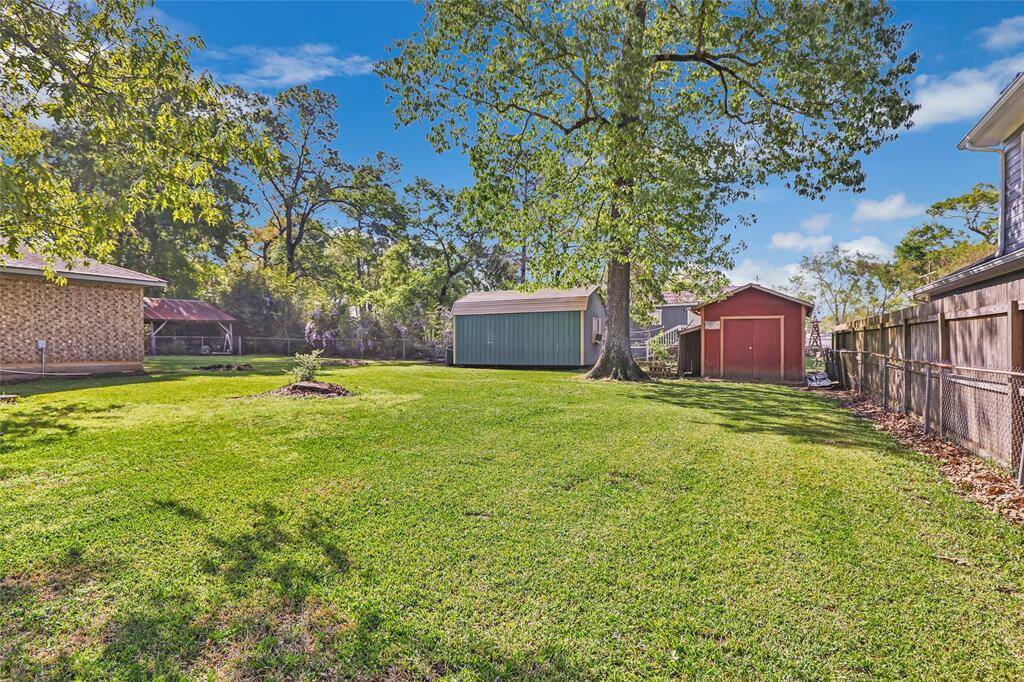 Spacious backyard with lush green grass, a large tree, and two storage sheds. The area is fenced and offering a private outdoor space.