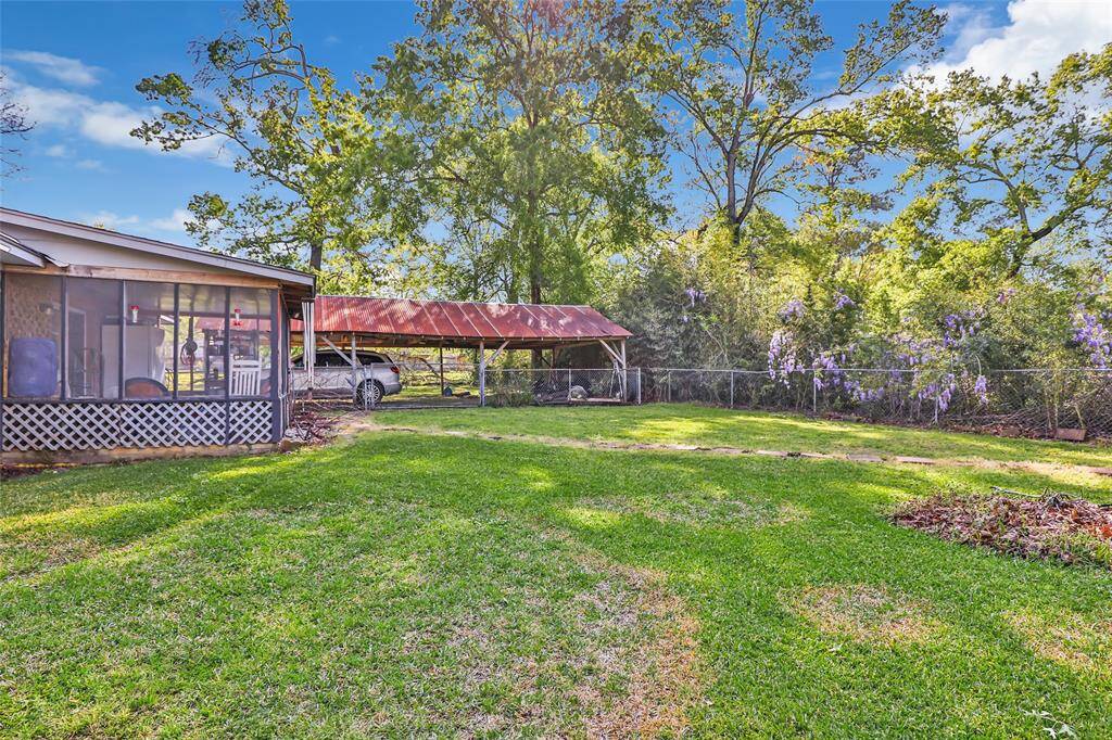 This photo showcases a spacious backyard with well-maintained grass, a sunroom, a carport, and mature trees providing shade and privacy. Perfect for outdoor enjoyment and relaxation.