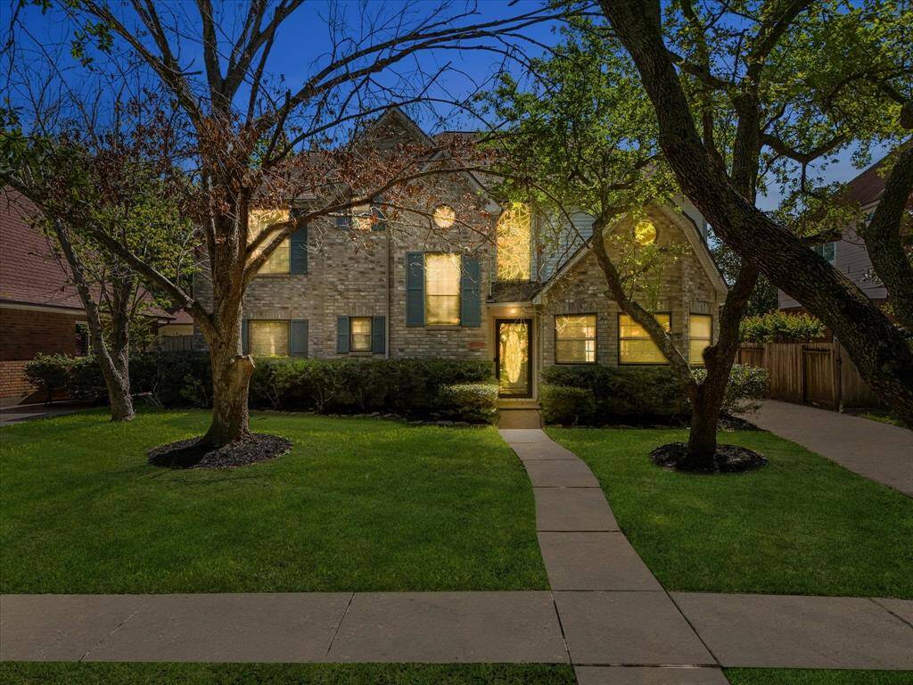 Welcome to 2919 Double Lake Ln! Stunning curb appeal with glowing evening ambiance, mature trees, and charming brick facade.