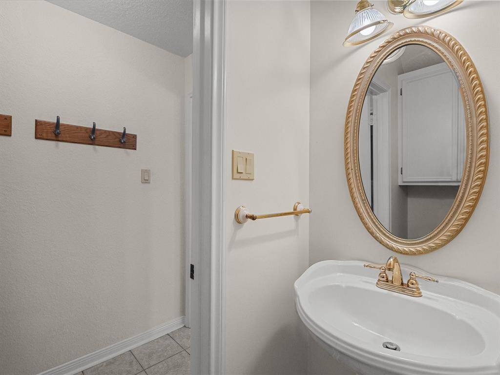 Convenient half bath with pedestal sink, elegant oval mirror, and stylish gold-tone fixtures.