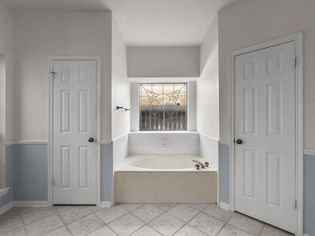 Garden tub framed by decorative glass window and two separate walk-in closets.