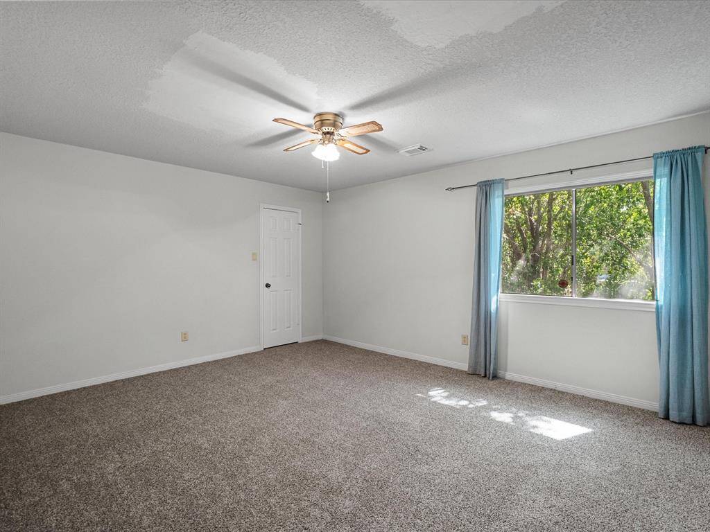 Oversized secondary bedroom with fresh carpet, ceiling fan, and a peaceful backyard view.