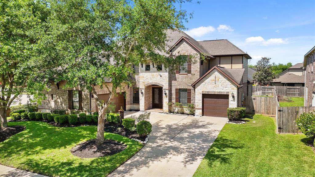 Charming two-story brick and stone house with a well-maintained front yard. The property features a spacious driveway, attached garage, and lush landscaping with mature trees.