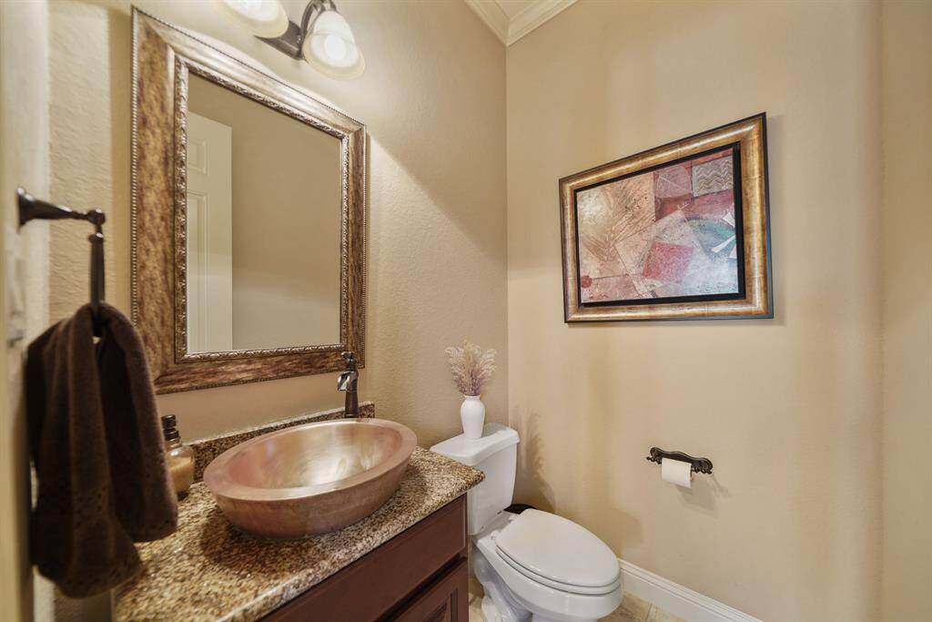 This is a stylish half-bathroom featuring a granite countertop with a unique copper vessel sink. It has warm beige walls, a decorative framed mirror, and modern lighting, creating an elegant and cozy atmosphere.