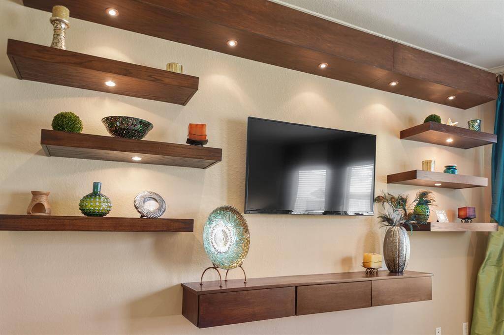 This modern living space features a sleek, wall-mounted TV surrounded by stylish floating shelves with recessed lighting.
