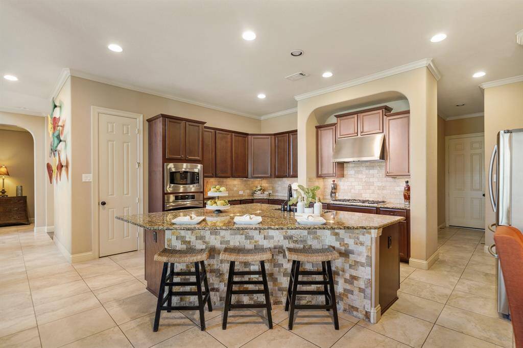 This kitchen features a spacious layout with a large island, granite countertops, and rich wood cabinetry. It includes stainless steel appliances, recessed lighting, and a stylish tile backsplash, creating a modern and inviting cooking space.