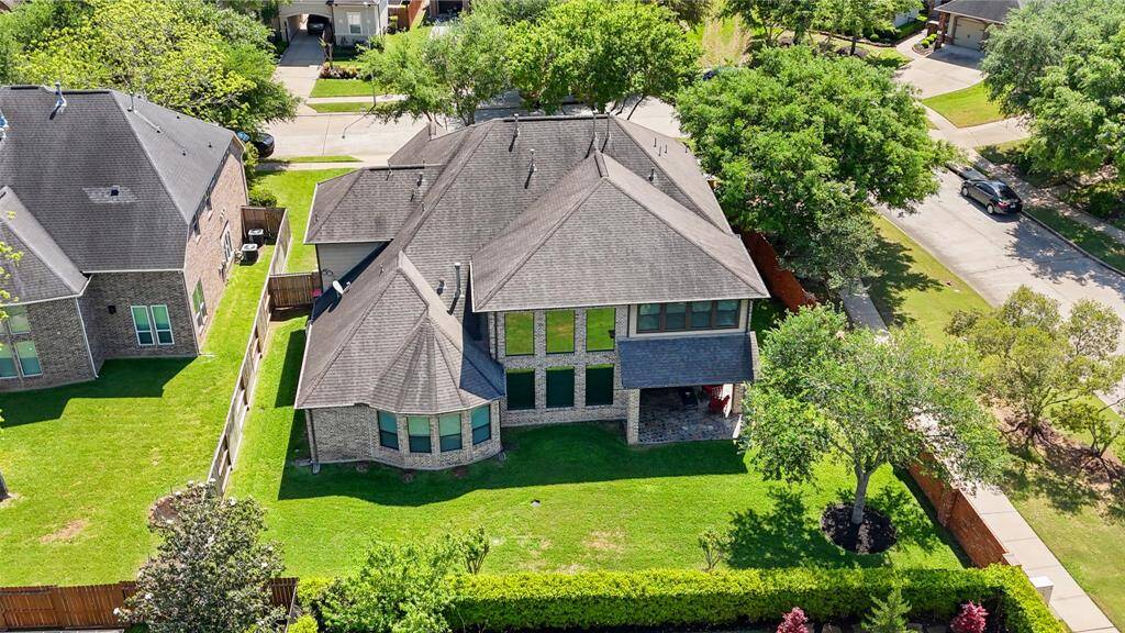 This photo showcases a spacious two-story home with a large, well-maintained backyard. The house features a modern roof design and ample windows for natural light. It is situated in a suburban neighborhood with mature trees and a surrounding wooden fence for privacy.