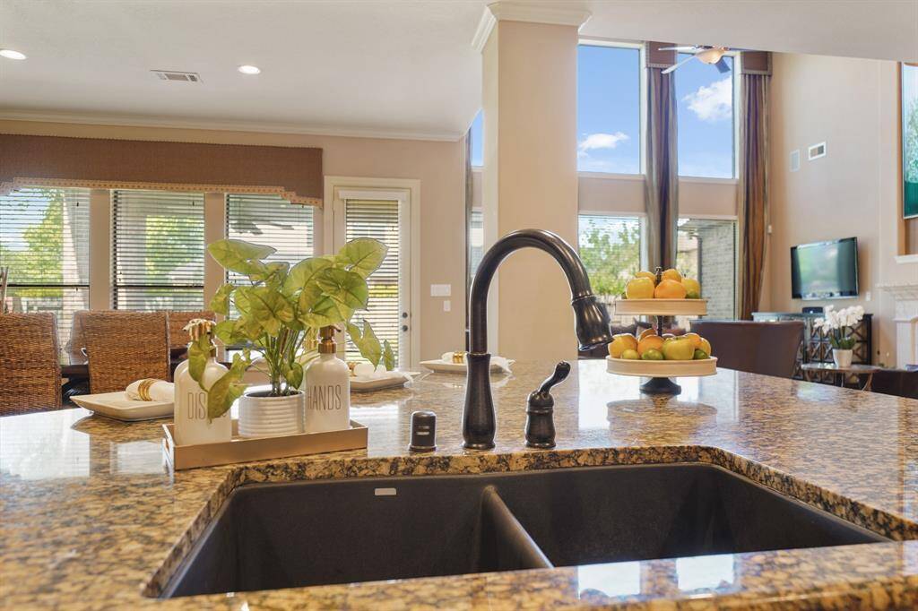 This photo showcases a bright and spacious kitchen with a granite countertop island, featuring a sleek black faucet. The open-concept design flows into a living area with large windows, offering plenty of natural light.