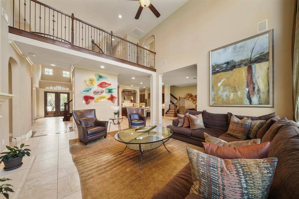 This spacious living area features a high ceiling and an open layout with a modern, elegant design. A balcony overlooks the space, and the room is filled with natural light from the large windows, offering a welcoming atmosphere.