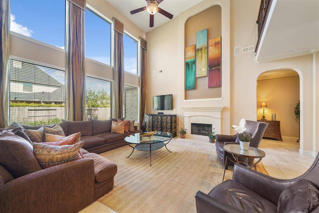 This spacious living room features high ceilings and large windows that allow ample natural light. It includes a cozy fireplace, perfect for relaxation or entertaining guests.