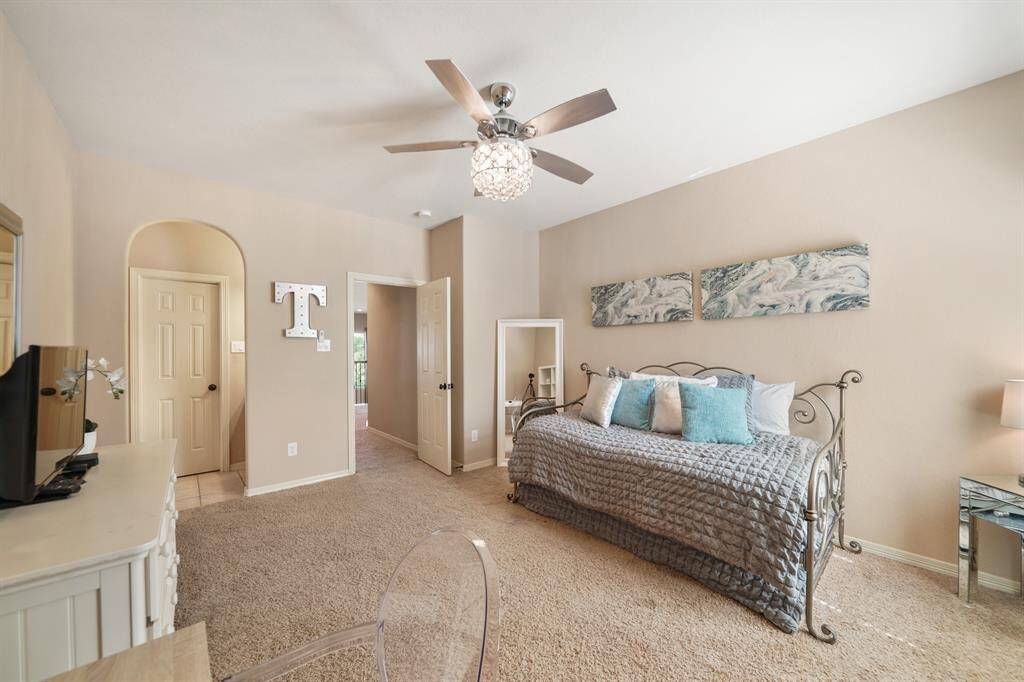 This cozy bedroom features neutral tones and carpeted flooring, with a stylish ceiling fan and ample natural light.