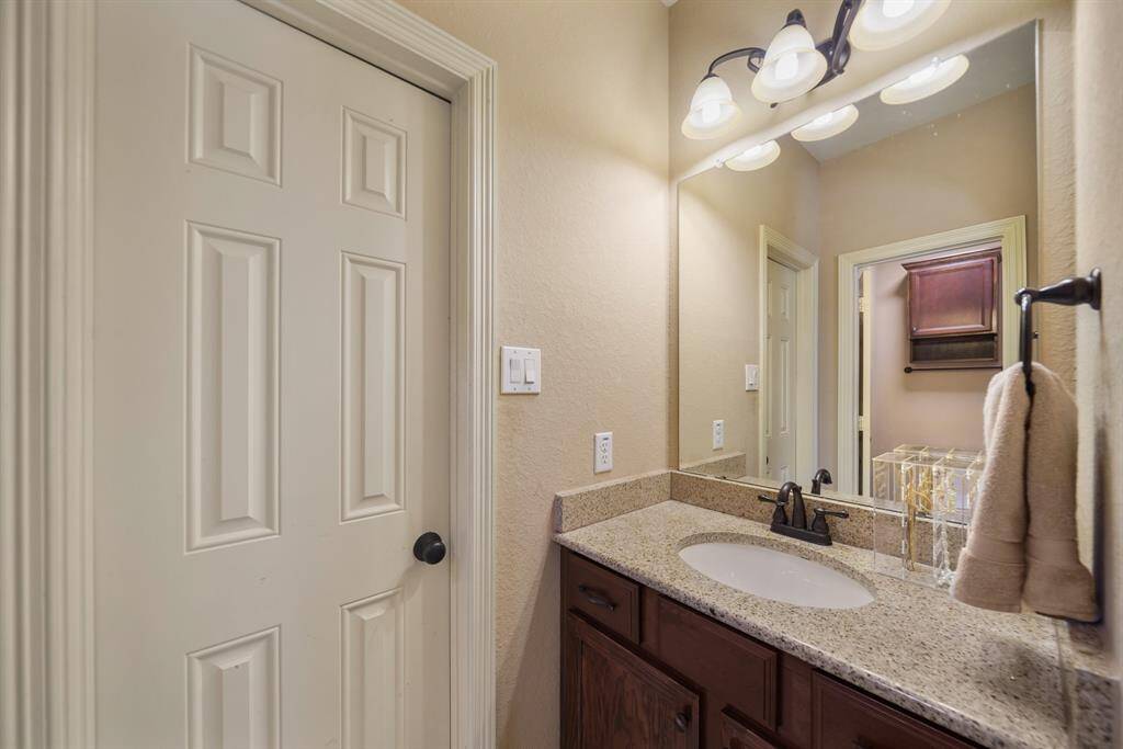 This photo showcases a cozy bathroom featuring a granite countertop with an undermount sink, warm lighting, and a wooden vanity.