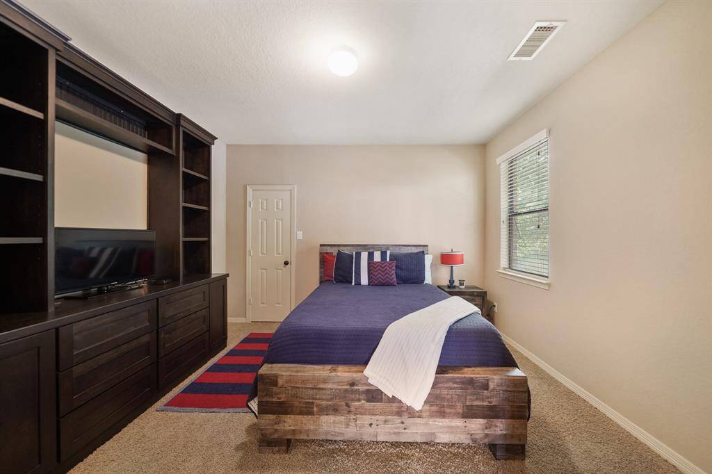 This cozy bedroom features a modern wooden bed, a large built-in entertainment center with ample storage, and neutral walls. A window provides natural light, complementing the room's warm ambiance.