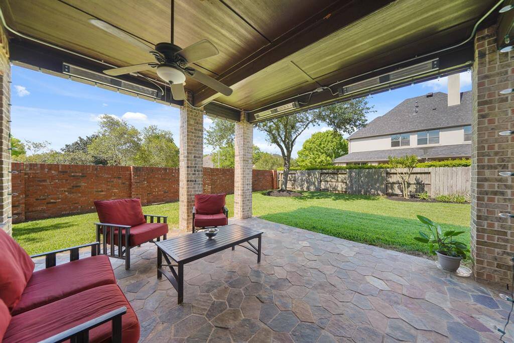 This photo showcases a spacious covered patio with a ceiling fan and comfortable seating, overlooking a well-maintained backyard with a brick and wooden fence, perfect for outdoor relaxation and entertaining.