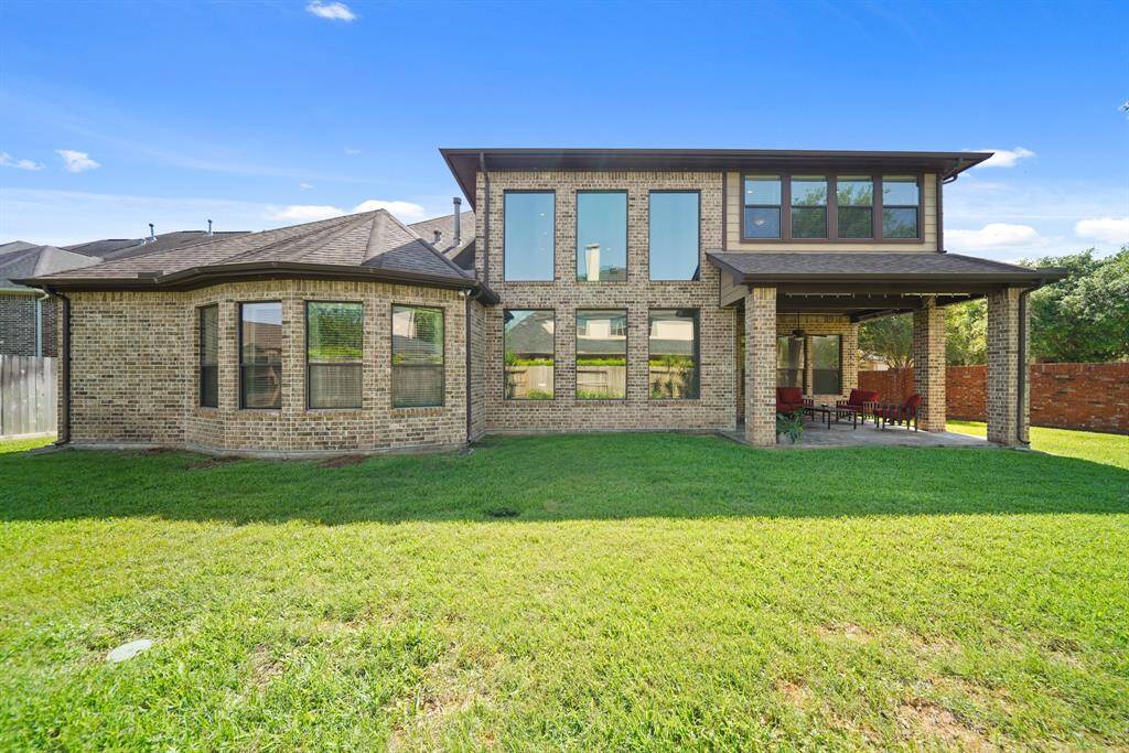 This is a two-story brick home with large windows and a covered patio. The backyard features a spacious lawn, perfect for outdoor activities and entertaining.